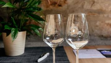 Two wine glasses on a wooden table with a potted plant and a stone wall in the background.