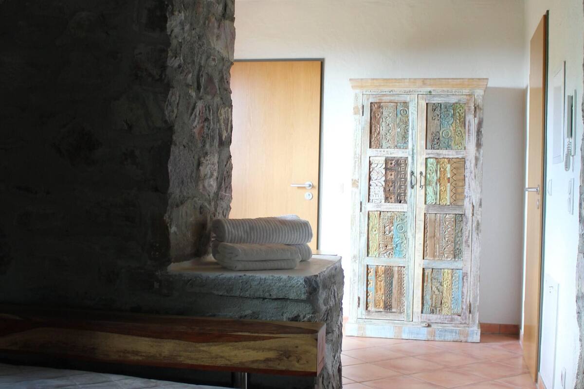 A bedroom with a stone archway, a bed, and a view of a door with patterned glass panels.