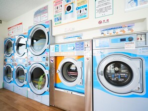 A row of multi-purpose washers and dryers with instructional posters on the wall.
