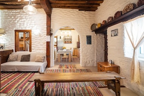 A rustic room with a wooden bench, a sofa, a dining table, and a kitchen area visible through an archway.