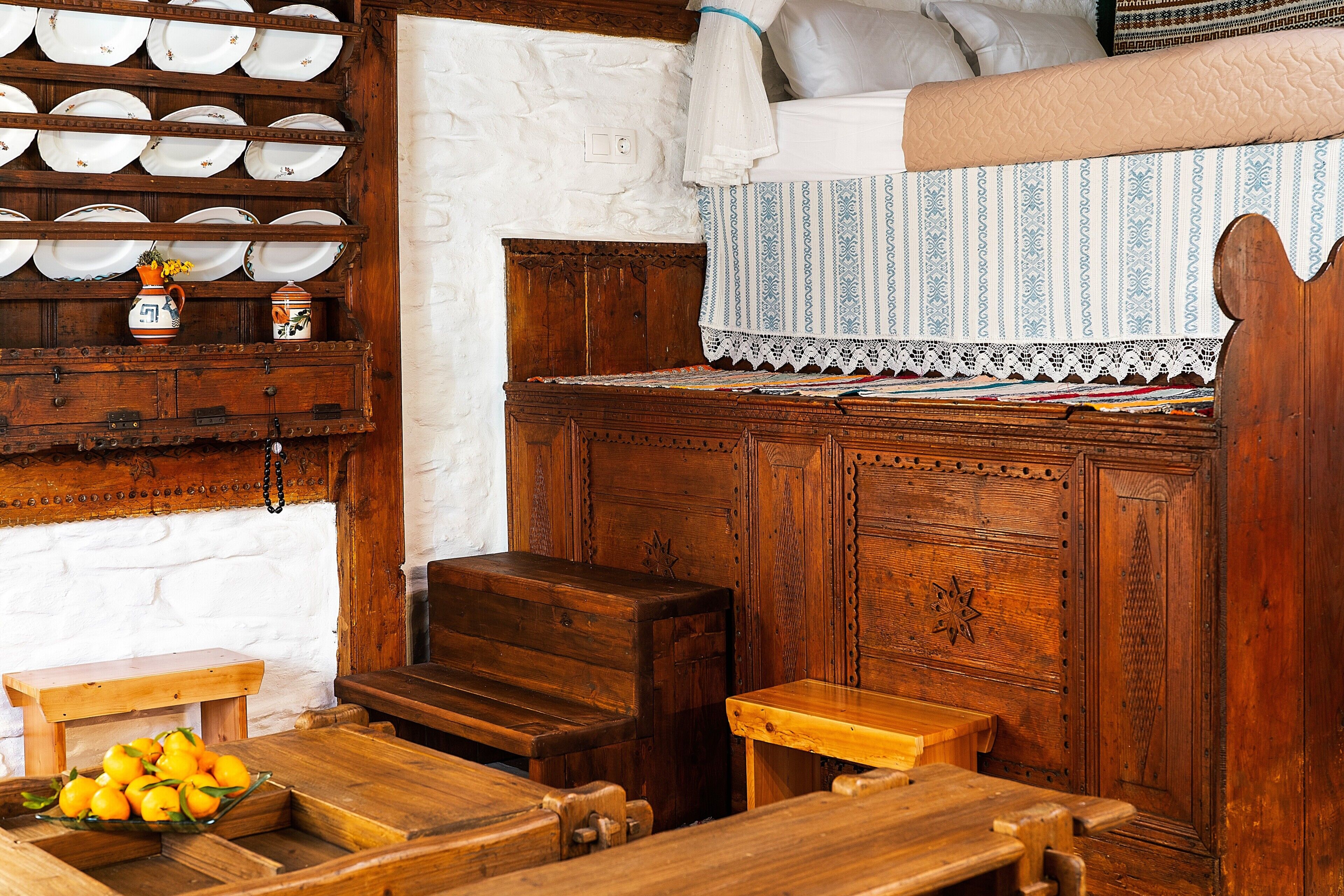 Una habitación rústica con muebles de madera, un banco, una mesita con un frutero y una estantería con platos y un jarrón.