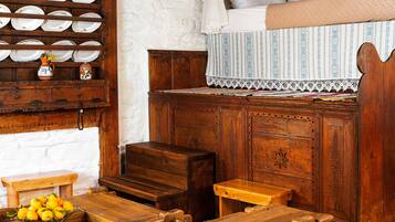 Una habitación rústica con muebles de madera, un banco, una mesita con un frutero y una estantería con platos y un jarrón.