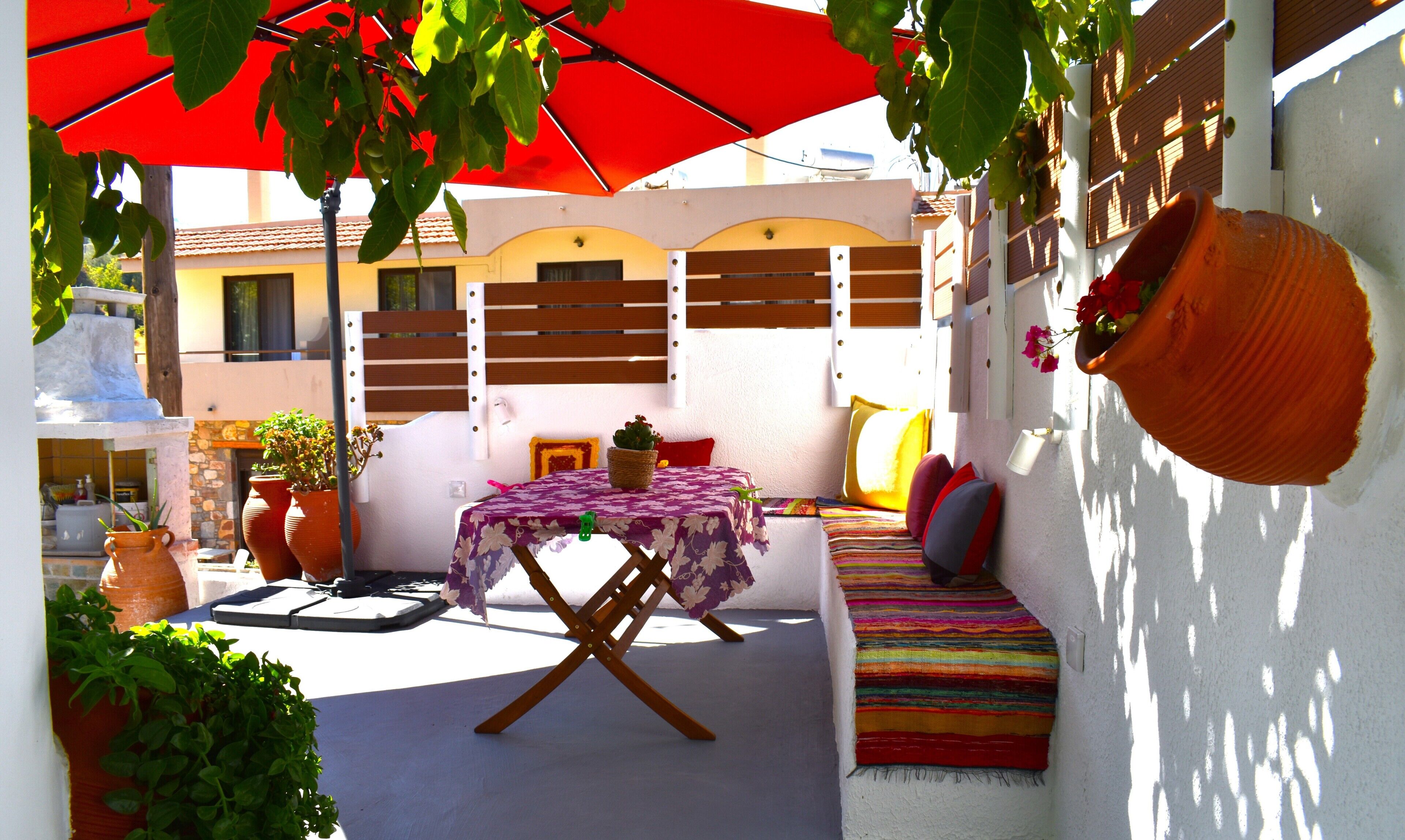 Une terrasse avec une table, des chaises et un parasol rouge.