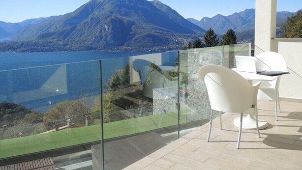 Un balcon doté d’une balustrade en verre, de chaises blanches et offrant une vue sur une montagne et un lac.