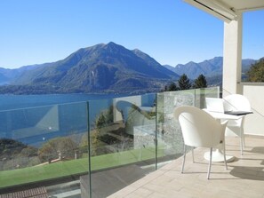 Ein Balkon mit Glastrennwand, weißen Stühlen und Blick auf einen Berg und See.