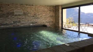 Un bain à remous avec un mur en pierre en arrière-plan, une fenêtre et une vue sur les montagnes.