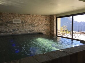 Un jacuzzi con un muro de piedra de fondo, una ventana y vistas a las montañas.