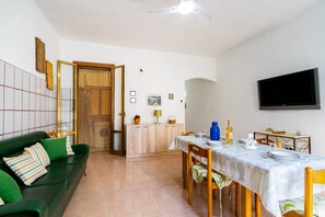 A dining area with a table set for four, a sofa, a television, and a cabinet with decorative items.