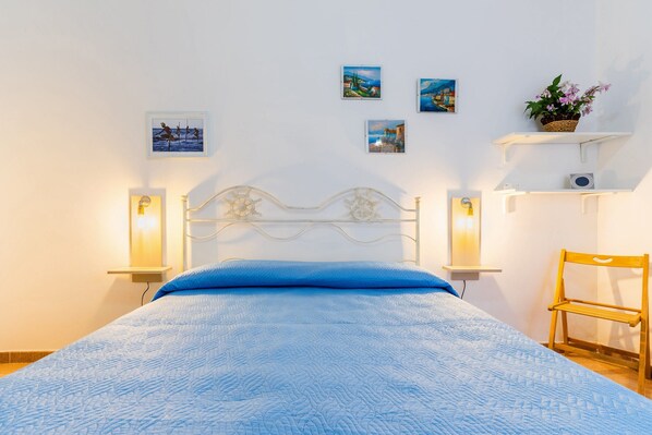 A bedroom with a bed, wall-mounted artwork, a shelf with a plant, and a chair.