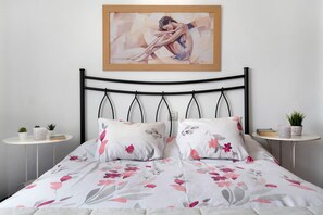 Una cama con ropa de cama floral, un cuadro enmarcado encima y dos mesitas de noche con plantas.