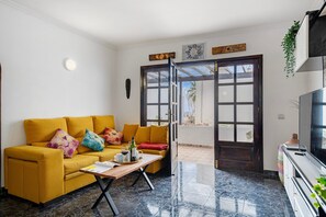 Una sala de estar con un sofá, una mesa de centro, un televisor y una puerta que da a un espacio al aire libre.