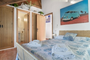 Un dormitorio con cama, toallas, un cuadro de una furgoneta, armario de madera y una puerta que da a un baño.