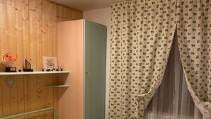 Une pièce avec un lit, un mur en bois, une étagère où sont exposés des trophées et un rideau orné d’un motif floral.