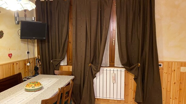 Un coin repas comprenant une table, des chaises, un téléviseur et une fenêtre avec des rideaux.
