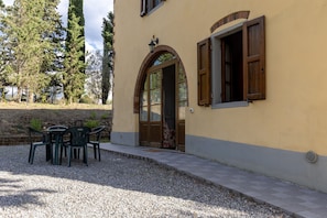 A building with a door, windows, and a small outdoor seating area with tables and chairs.