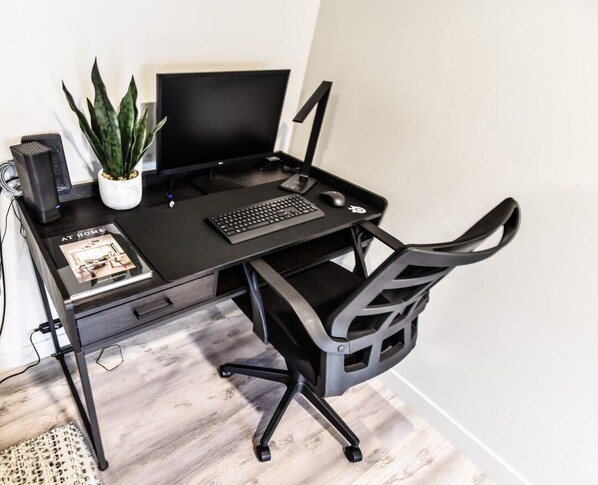 A black desk with a computer, keyboard, and mouse. There is a potted plant and a book on the desk.