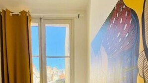 Ein Zimmer mit einem großen Fenster, einem Heizkörper, einem Holzboden und einem Gemälde an der Wand.