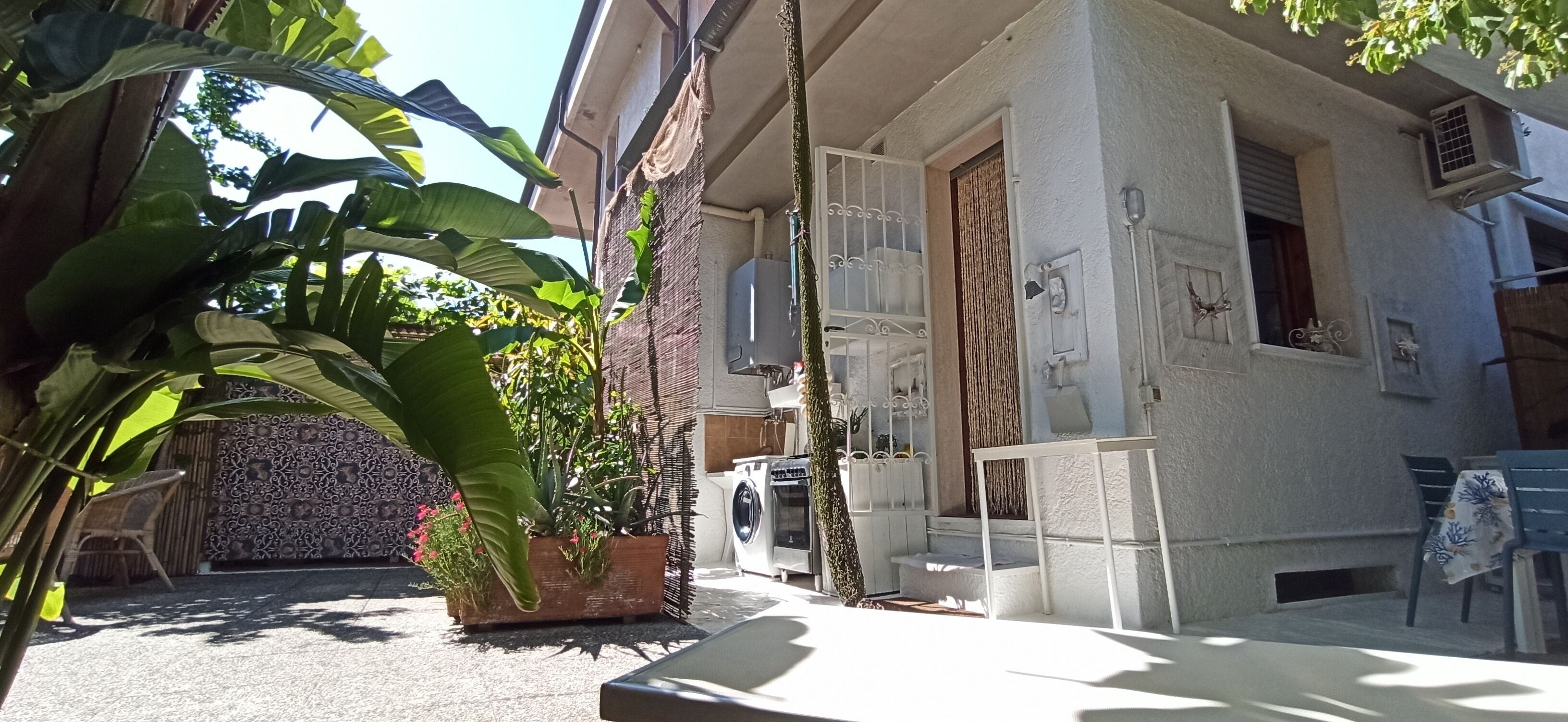 Un immeuble résidentiel doté d’un espace buanderie, d’un petit coin salon extérieur et d’une grande plante en pot.