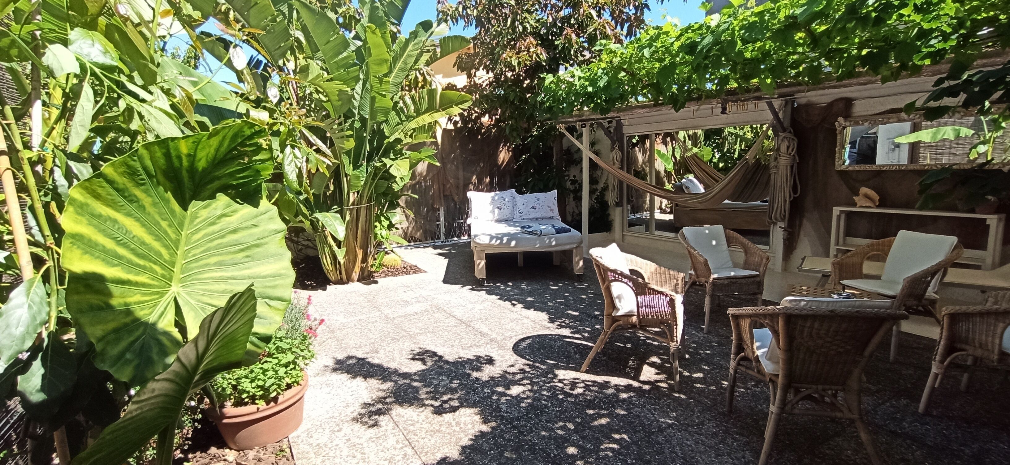 A garden patio with a hammock, wicker furniture, and a bed.