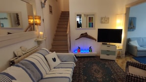 A living room with a striped sofa, a television, a staircase, and a wall-mounted shelf with decorative items. - Simone Mare (CIN: IT046033C2FHIIU2HV) (Torre del Lago Puccini)