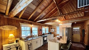 A rustic kitchen with wooden beams, a marble island, white cabinetry, and a built-in stove.