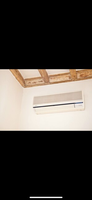 A white air conditioning unit mounted on a wall with exposed wooden beams above.