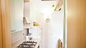 A narrow kitchen with white cabinets, a gas stove, and a clock on the wall. - Loft in The heart of Ancient Rome (Roma)