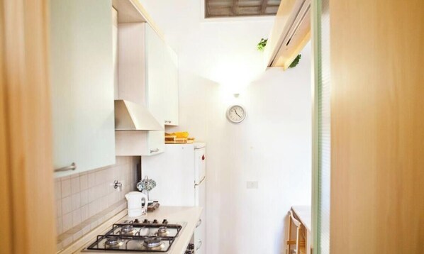 Une cuisine étroite avec des meubles blancs, une cuisinière à gaz et une horloge au mur.