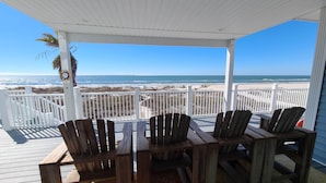 A covered outdoor seating area with wooden chairs and a table, overlooking a beach with a white fence and palm tree. - Beachfront home with beautiful view of beach and ocean. (Port St. Joe)