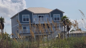 A two-story house with a balcony, surrounded by tall grasses and palm trees. - Beachfront home with beautiful view of beach and ocean. (Port St. Joe)