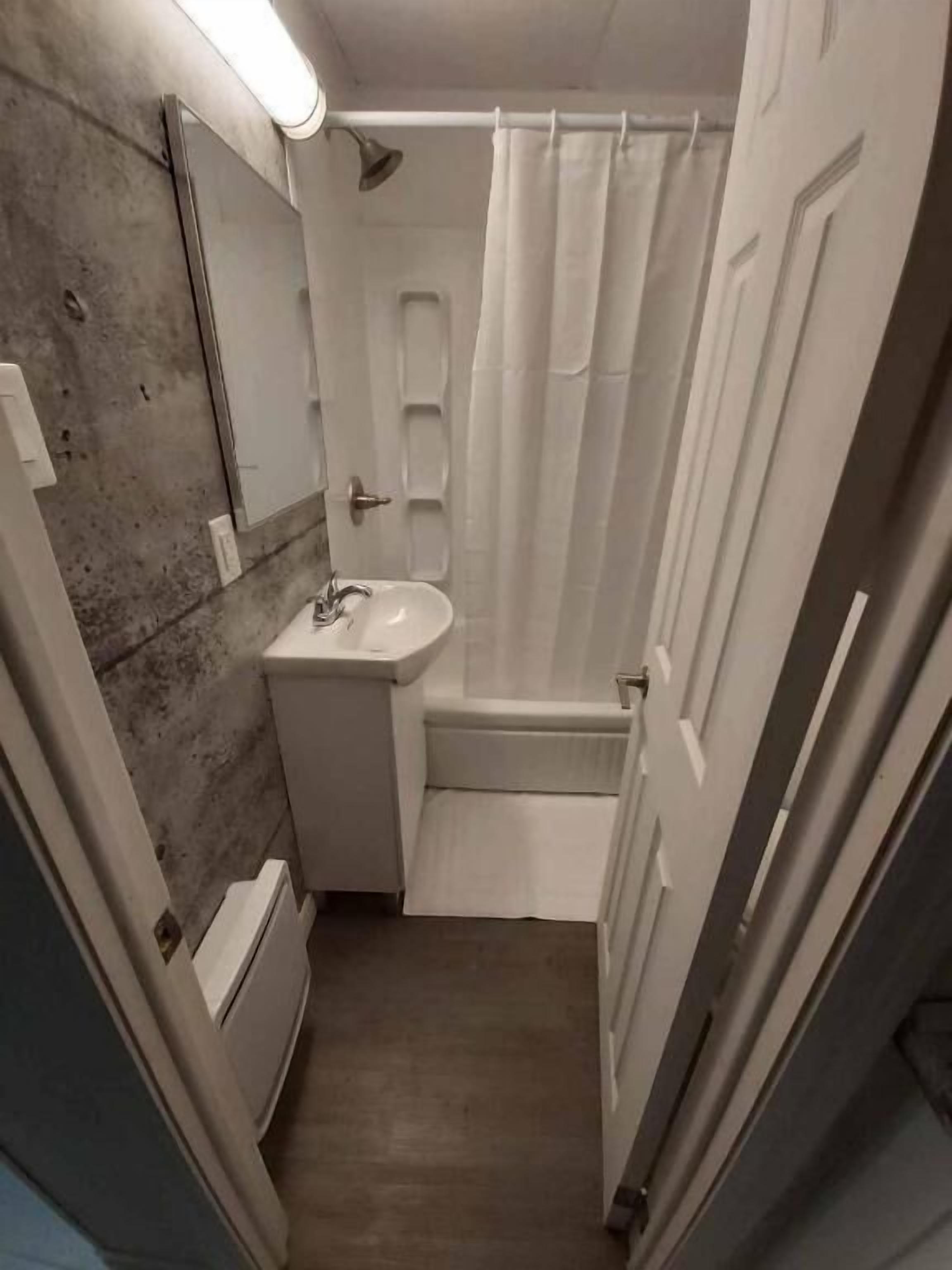 Een kleine badkamer met een wit wastafelmeubel, een spiegel, een douchegordijn en een deur.