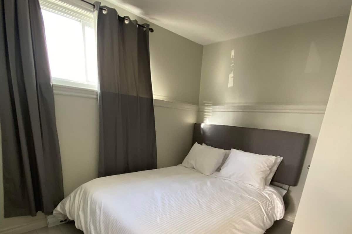 A neatly made bed with white bedding in a room with light wooden flooring and a dark headboard.