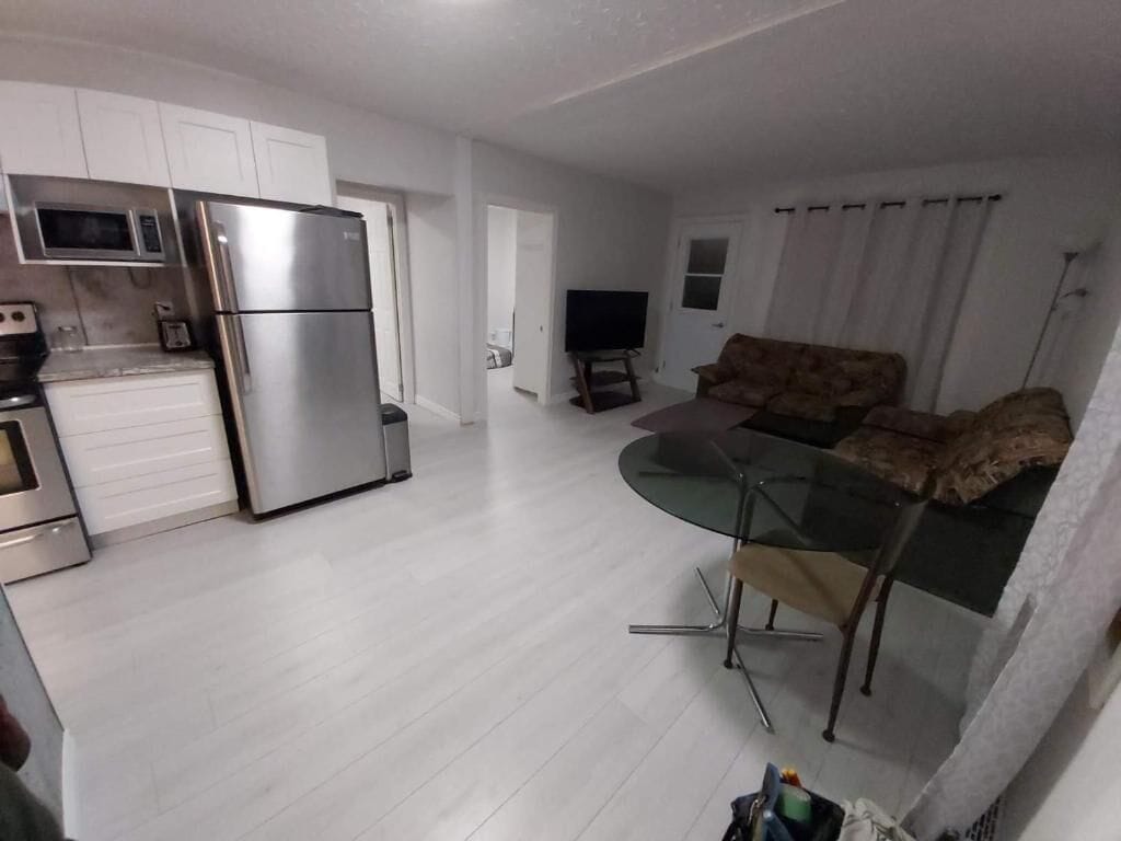 Una cocina moderna con electrodomésticos de acero inoxidable, un comedor con mesa de vidrio y una sala de estar con sofá.
