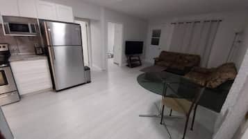 Una cocina moderna con electrodomésticos de acero inoxidable, un comedor con mesa de vidrio y una sala de estar con sofá.