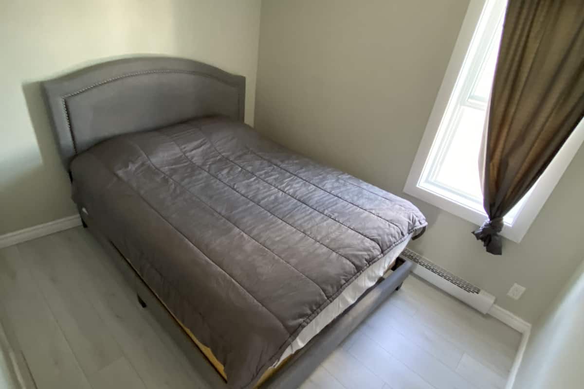 A bedroom with a bed, a window with curtains, and a radiator.