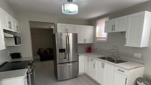 A modern kitchen with white cabinets, stainless steel appliances, and a light wood floor. - Le Cardinal (Rouyn-Noranda)