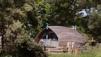 Une cabane en bois en forme de dôme, dotée d’une terrasse et d’une rambarde en bois, et entourée d’arbres.