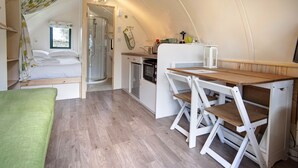 A compact, well-lit room with a bed, kitchenette, and a dining area. - Blackcleugh Glamping (Hexham)