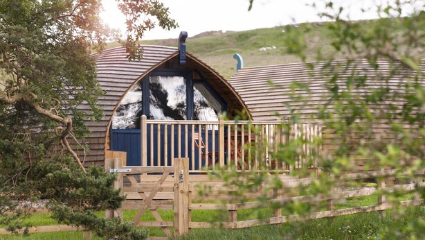 A wooden cabin with a sloped roof and a balcony, surrounded by greenery. - Blackcleugh Glamping (Hexham)