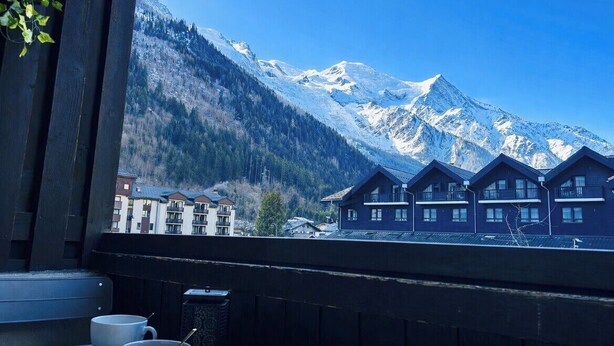 A mountain view with snow-capped peaks, a wooden balcony, and several chalet-style buildings.
