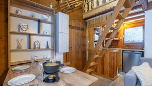 Ein gemütliches Holzhaus mit einem Esstisch für zwei Personen, einer Küchenzeile und einer Treppe zu einer weiteren Ebene.