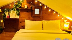 Ein gemütliches Zimmer mit einem Bett, einem Nachttisch, einer Lampe und einem kleinen Fenster mit Blick nach draußen.