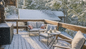 Ein mit Schnee bedeckter Deck mit Außenbestuhlung und Blick auf verschneite Bäume.
