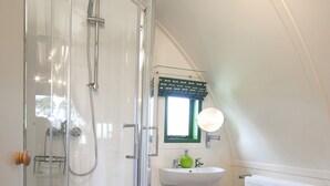 A modern bathroom with a glass-enclosed shower, a pedestal sink, and a small window above the mirror. - Barebones Glamping (Hexham)