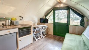 A compact kitchen with a refrigerator, stove, and a dining area with a table and chairs. - Barebones Glamping (Hexham)