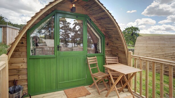 Une cabane en bois avec une porte verte, une petite table et une chaise sur une terrasse en bois.