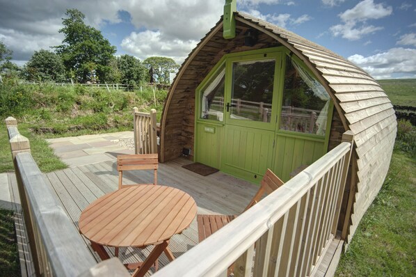 A wooden dome-shaped structure with a green door, a wooden deck with a table and chairs, and a view of the surrounding landscape. - Humbleton Glamping (Hexham)