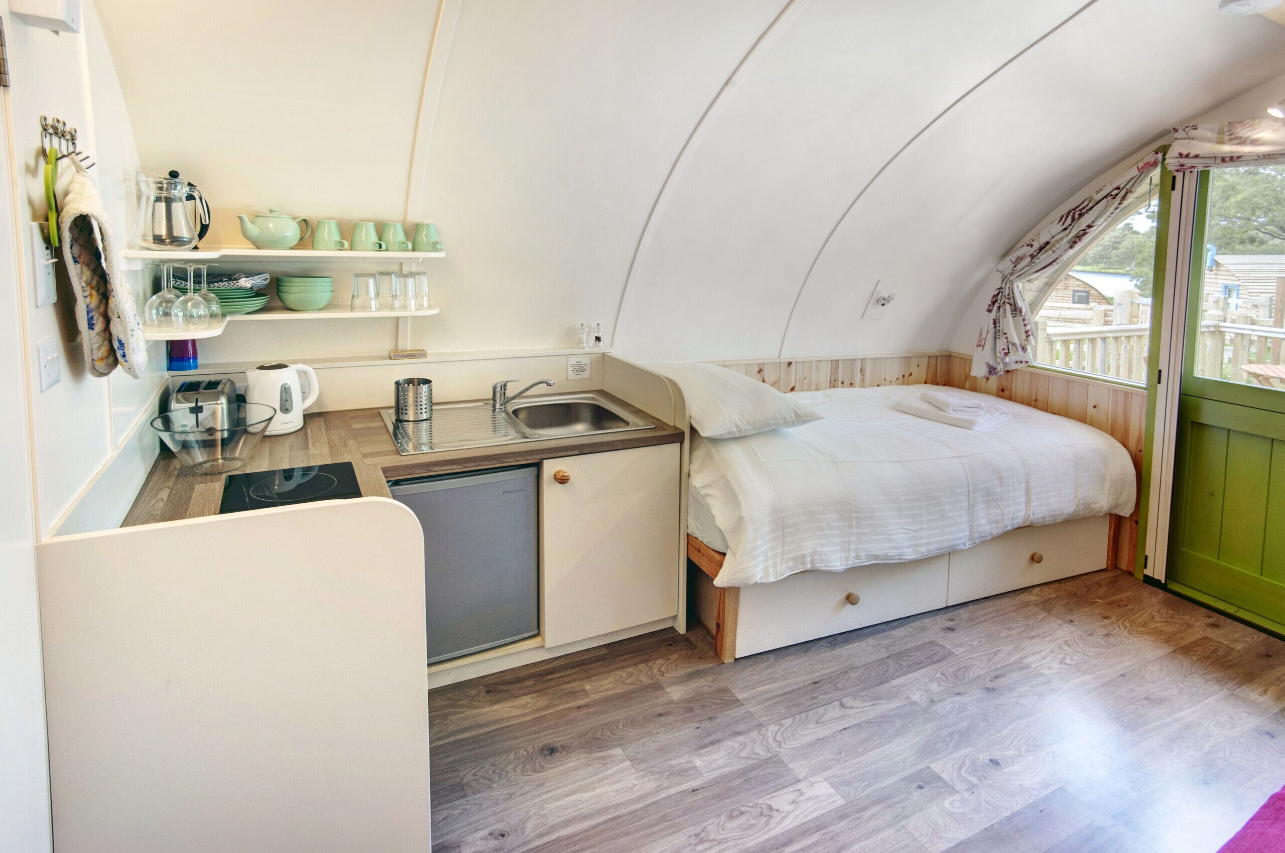 A compact, triangular room with a kitchenette, a bed, and a window.