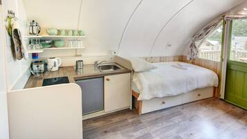 A compact, triangular room with a kitchenette, a bed, and a window.
