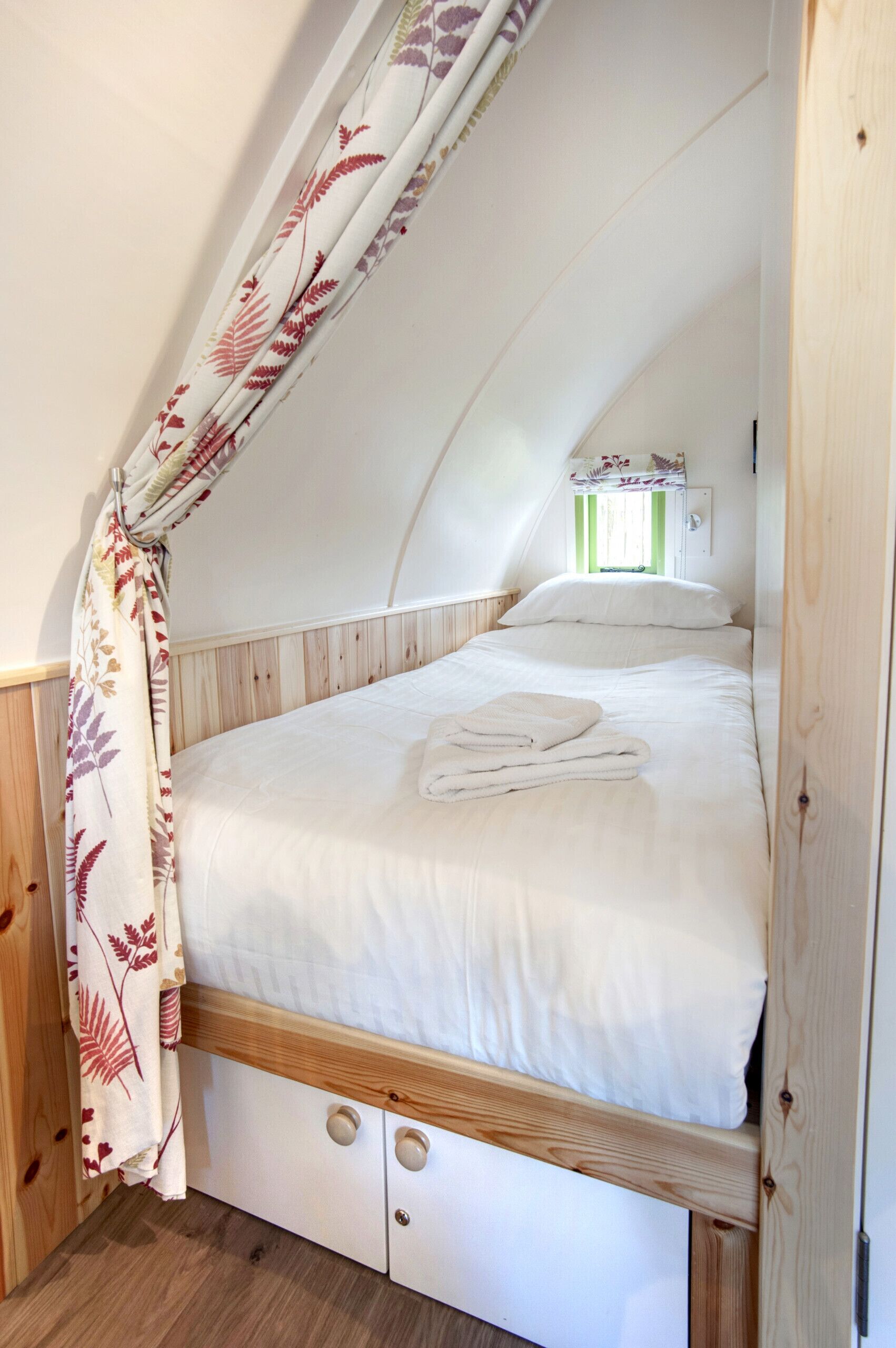 Une petite chambre à coucher accueillante, avec un lit simple, une tête de lit en bois et une fenêtre donnant sur un beau paysage.